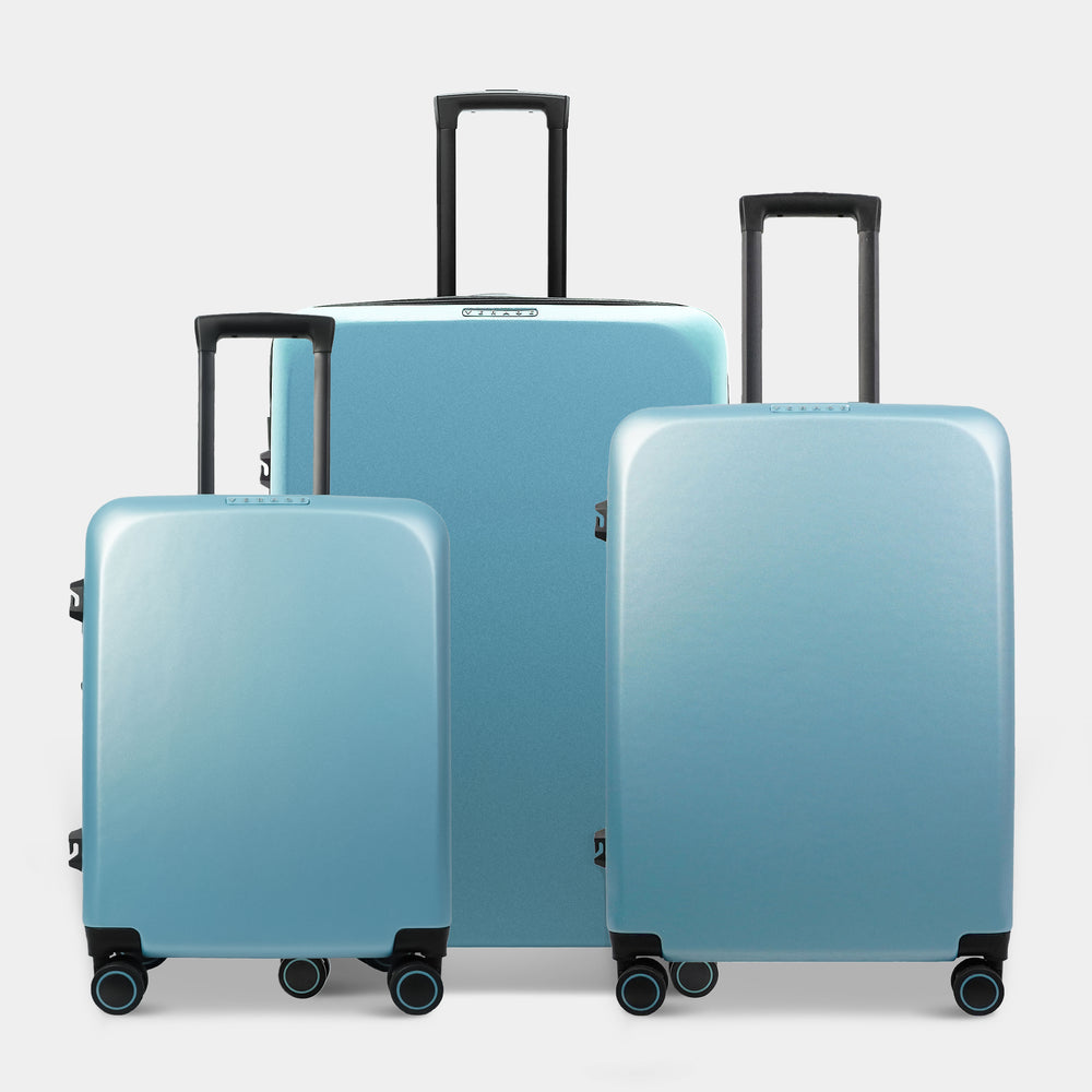 Three pieces of luggage in a gradient blue finish are displayed together. The set includes a large suitcase and two smaller ones, all featuring black trolley handles and wheels for easy mobility.