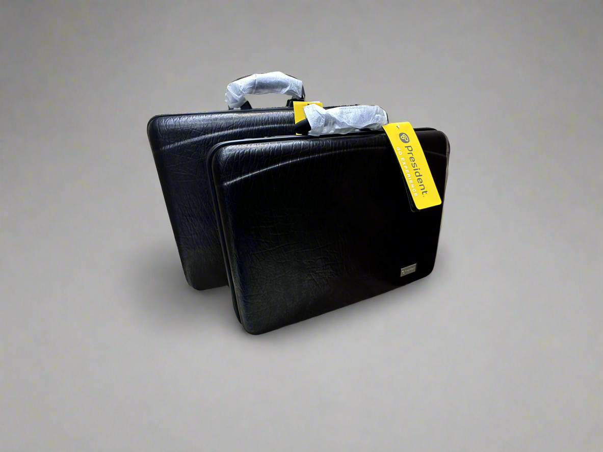 A sleek black President attache case is displayed, featuring a textured surface and dual handles. The case is shown with a yellow tag attached, emphasizing its design for durability and travel convenience.